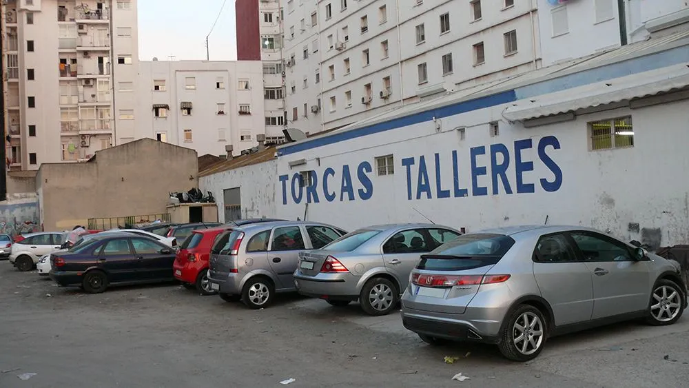 Campa del taller con una fila de coches aparcados junto a la nave, con el rótulo Torcas Talleres pintado en la pared.