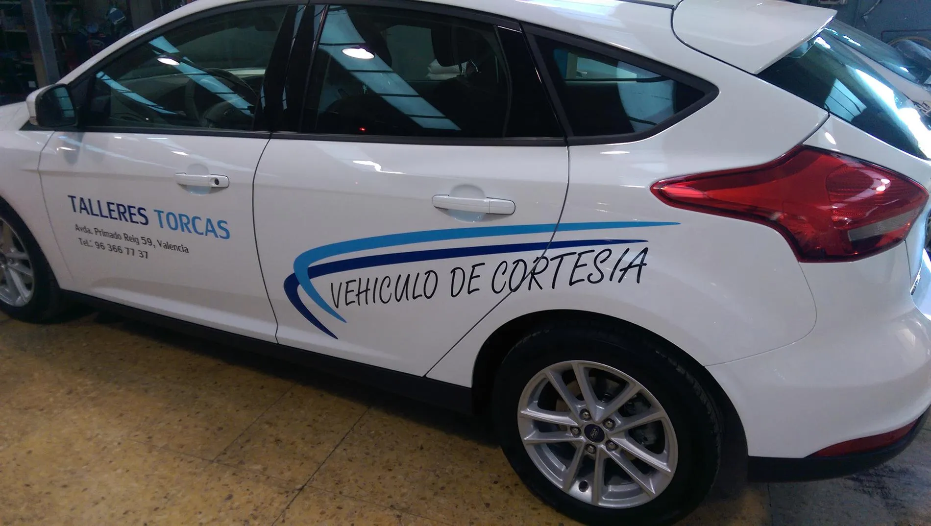 Ford Focus blanco rotulado con «Vehículo de cortesía», el nombre del taller, la dirección y el teléfono, dentro de la nave.