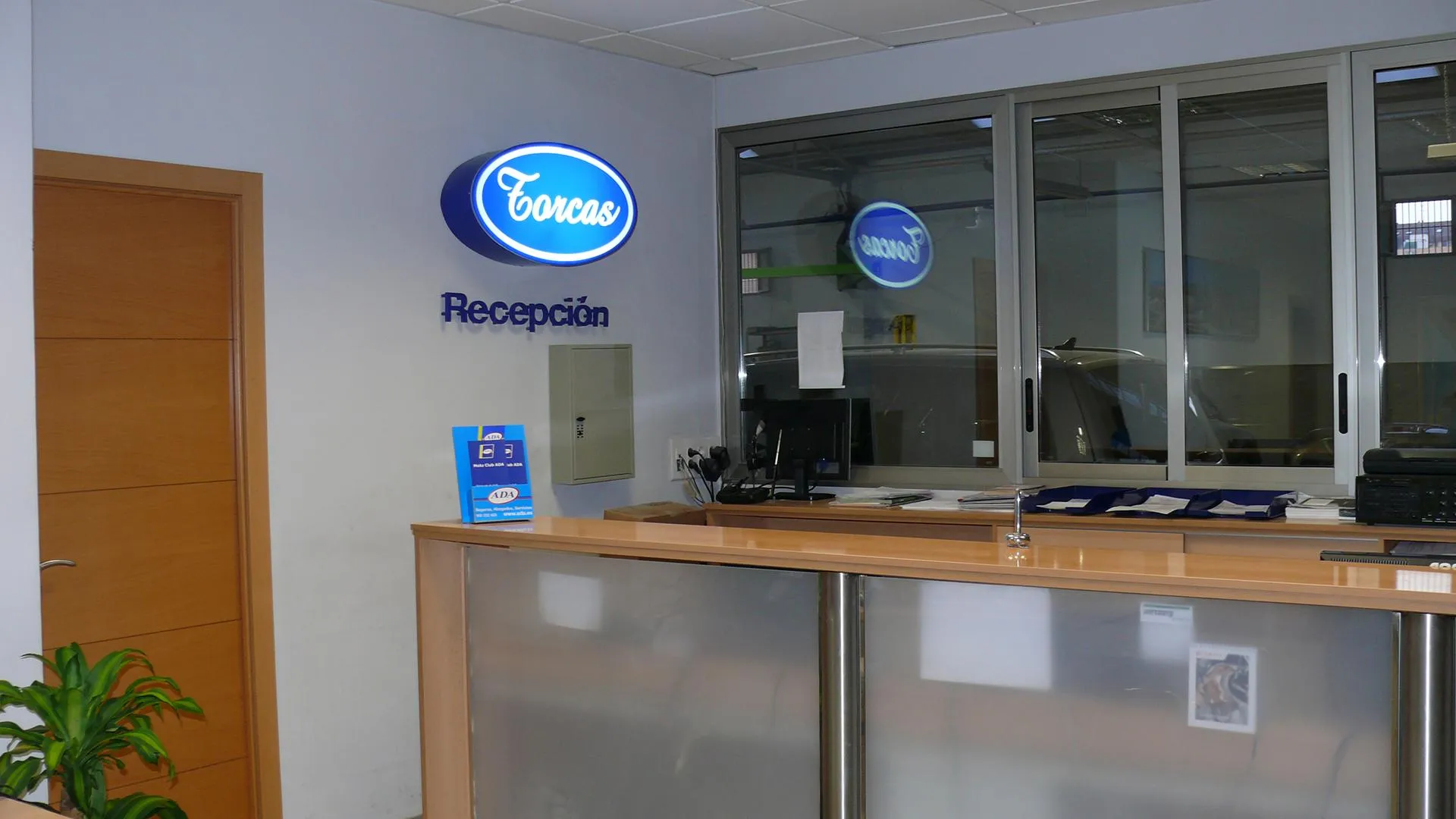 Mostrador de recepción del taller con el rótulo luminoso de Torcas en la pared.